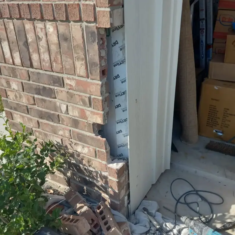 Brick removed beside an exterior door frame, with the sheathing exposed, before rebuilding
