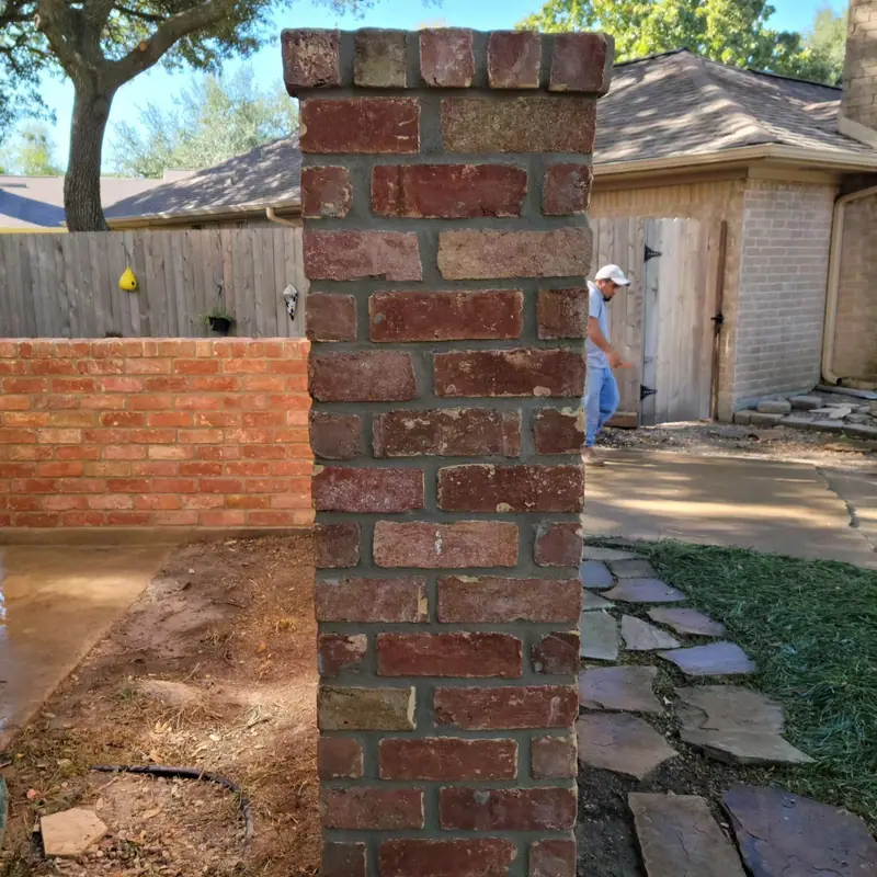 Rebuilt brick column beside a courtyard wall and flagstone path