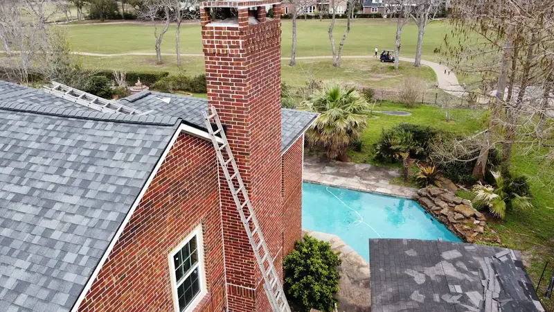 Tall exterior brick chimney on a two-story brick home beside a backyard pool