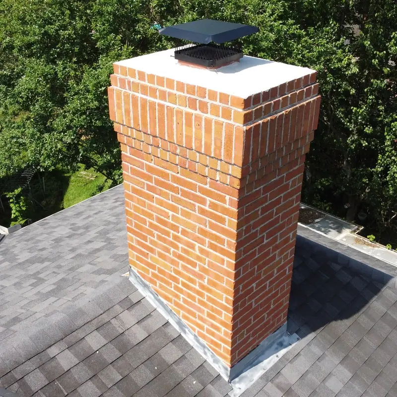 Red brick chimney with a black metal cap and fresh flashing at the roofline