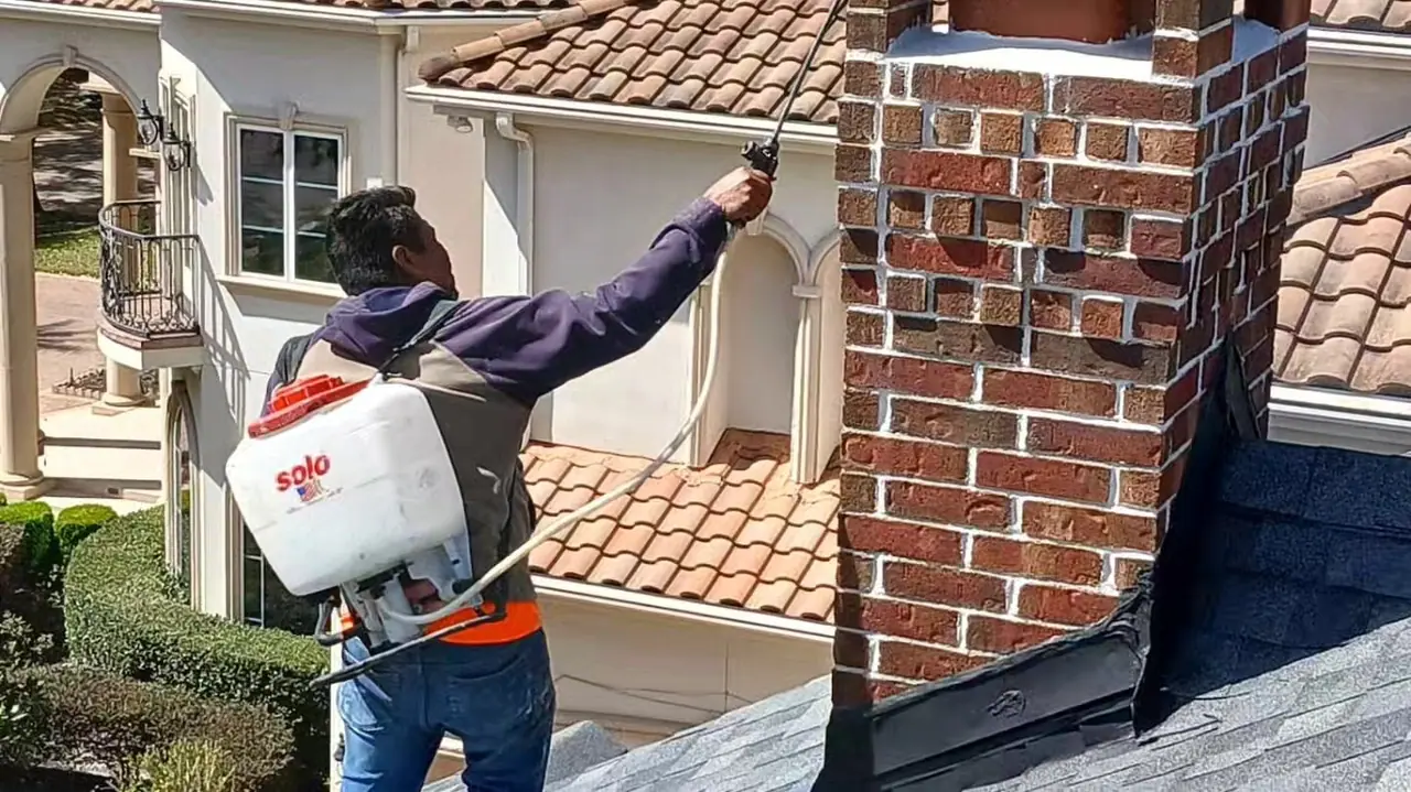 Crew member spraying a masonry water-repellent treatment onto a brick chimney