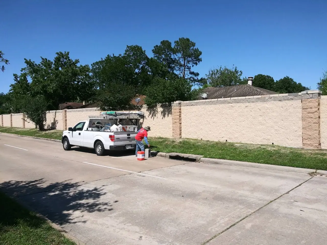 Long concrete block wall along a residential street, with a Houston Pro Masonry truck parked in front