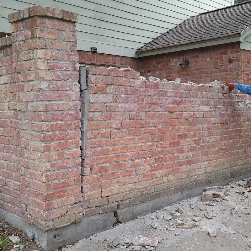Courtyard brick wall pulling away from its column, with broken brick at the base