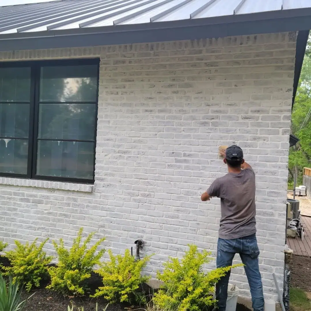 Crew member applying a finish to white brick on a modern home with a metal roof
