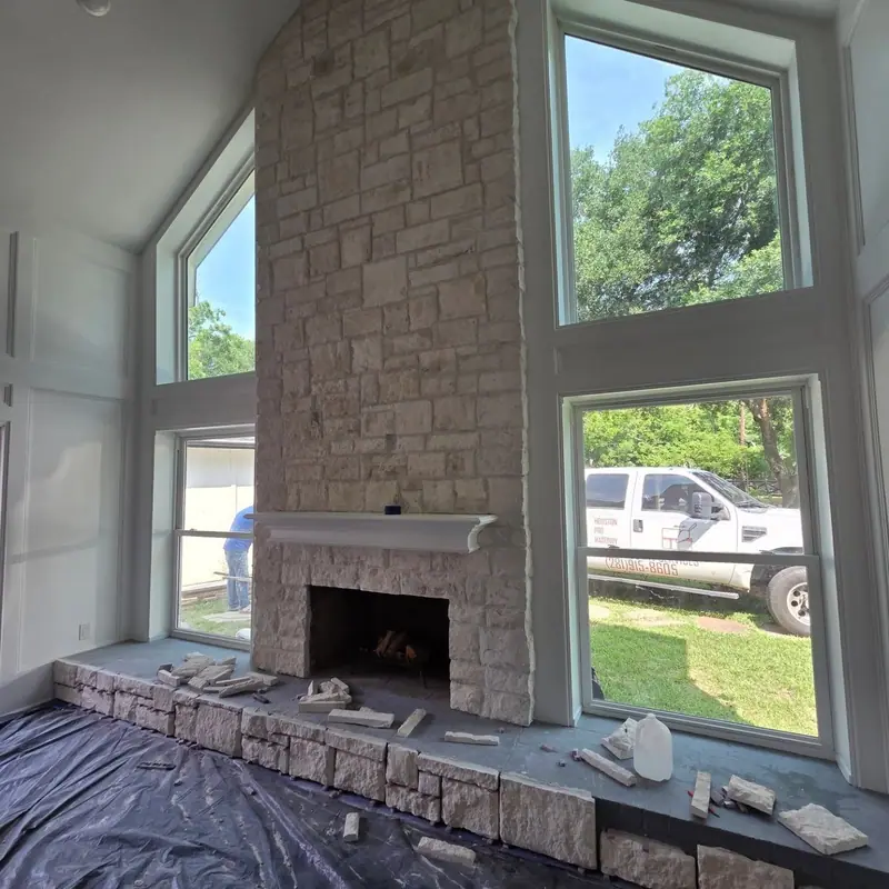 Two-story stone fireplace wall under construction, with the floor protected by plastic sheeting