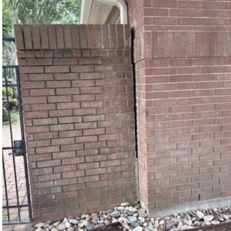Gap opening between a brick garden wall and a brick column beside an iron gate