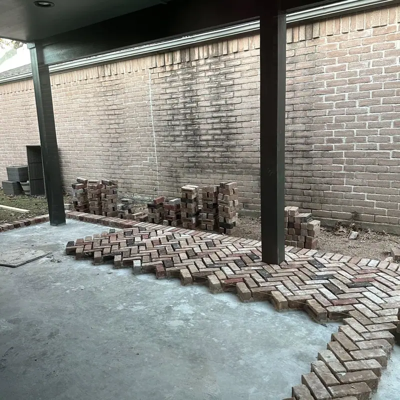 Herringbone brick pavers being laid on a covered patio beside a light brick wall