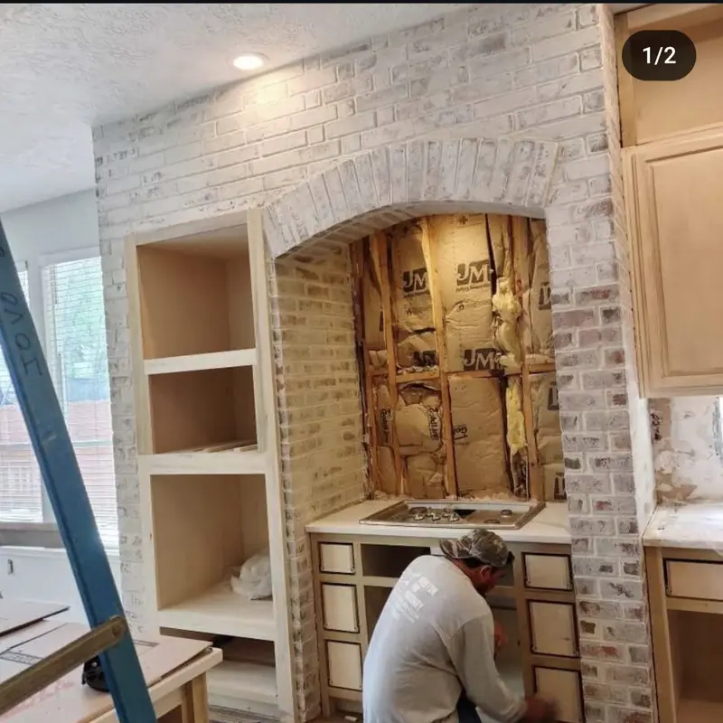Mason working inside an arched brick niche with a light finish, beside built-in cabinets