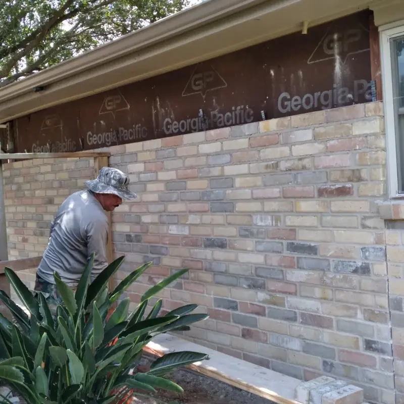Mason laying brick on an exterior wall below exposed sheathing