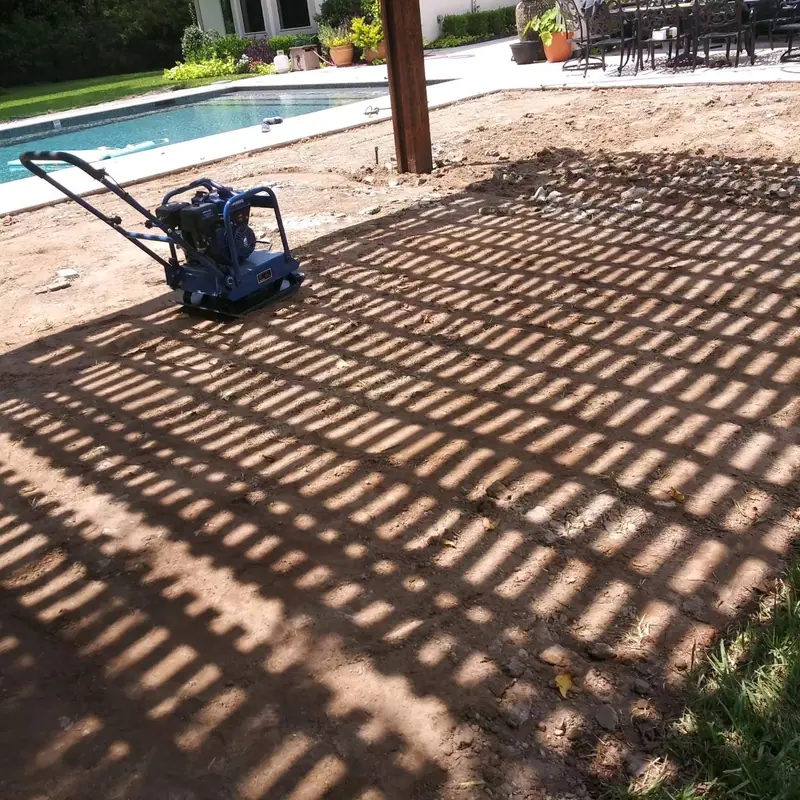 Plate compactor on a prepared base before pavers are set, beside a pool