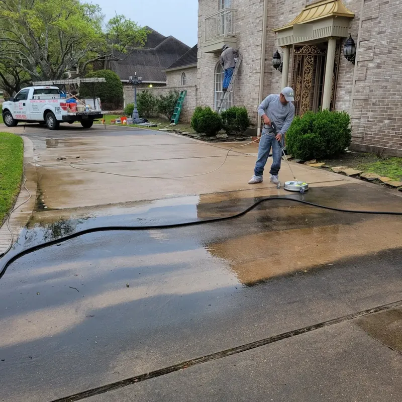 Crew member pressure washing a driveway, with the cleaned and uncleaned sections side by side