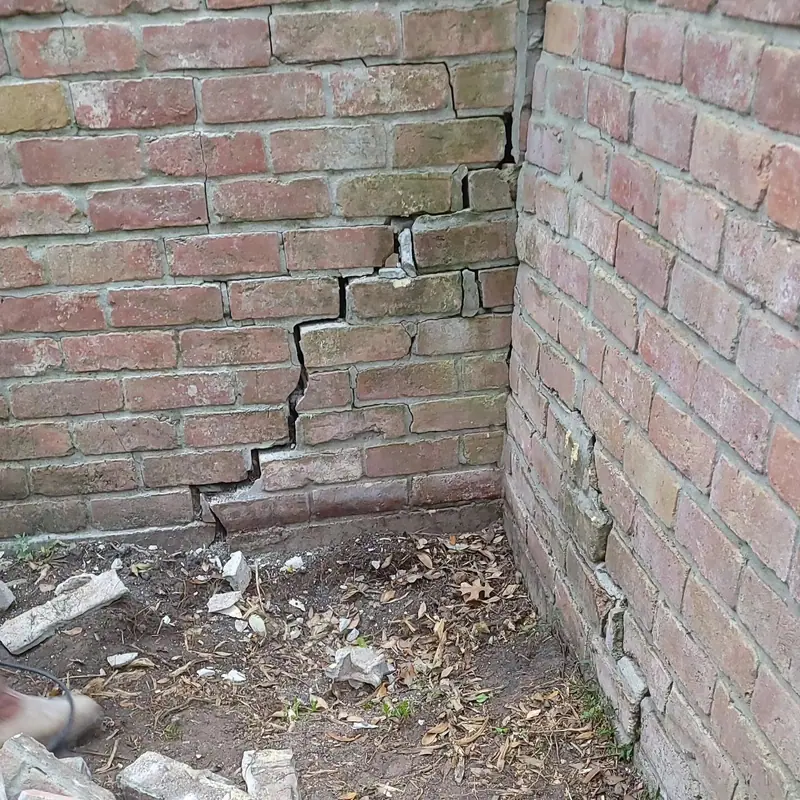 Stair-step crack running up through the mortar joints at the corner of a red brick wall